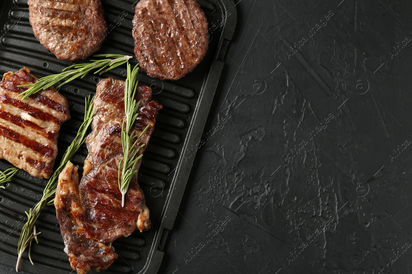 Photo of Delicious grilled beef meat with rosemary on black textured table, top view. Space for text