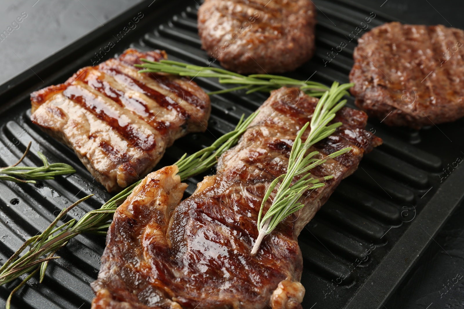 Photo of Delicious grilled beef meat with rosemary on black table, closeup