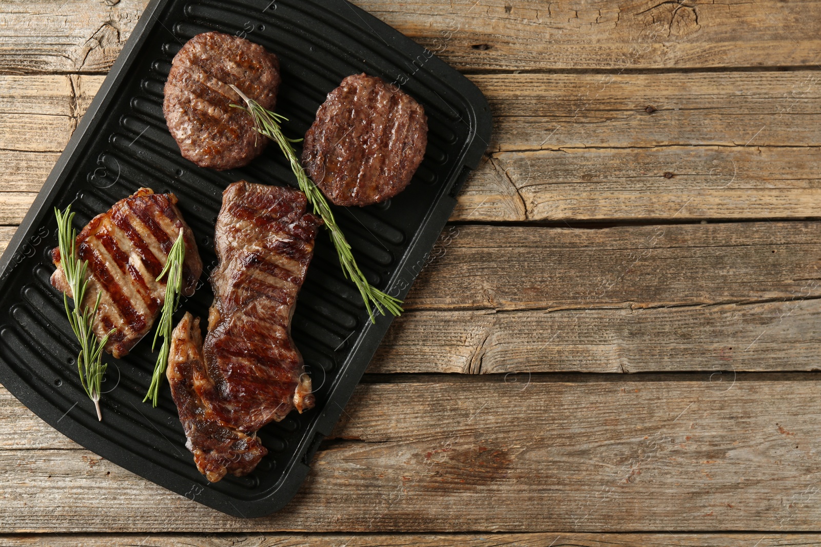Photo of Delicious grilled beef meat with rosemary on wooden table, top view. Space for text