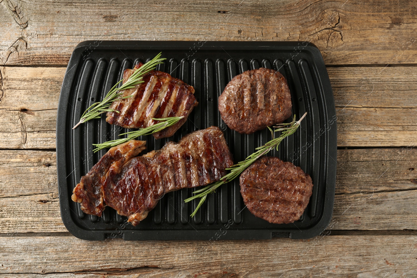 Photo of Delicious grilled beef meat with rosemary on wooden table, top view