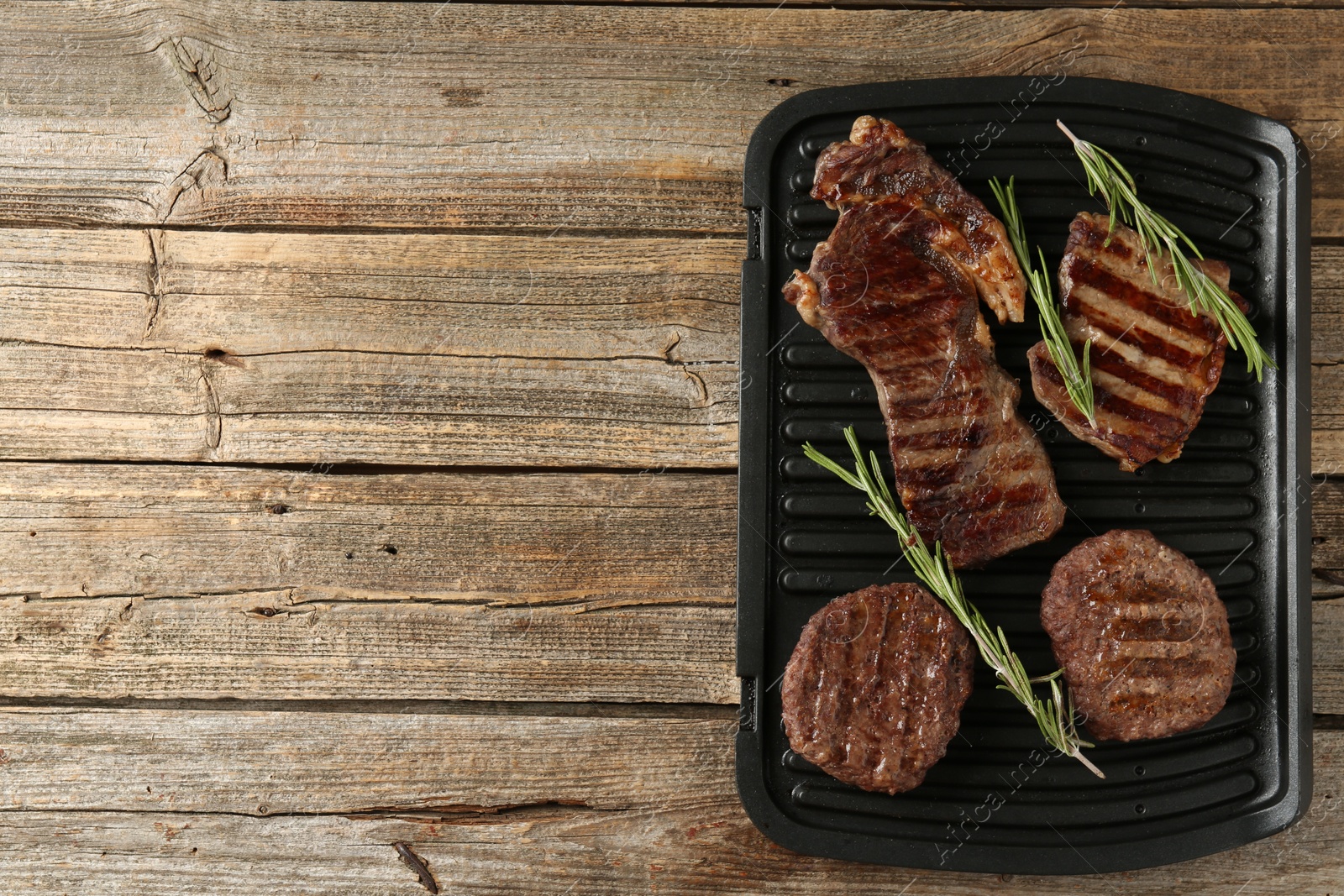 Photo of Delicious grilled beef meat with rosemary on wooden table, top view. Space for text