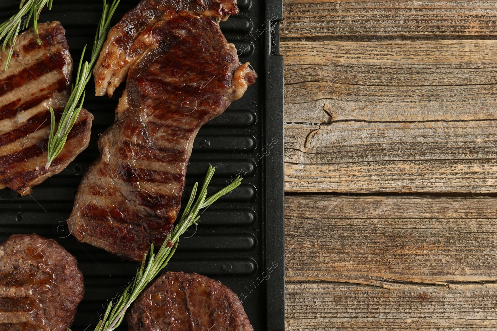 Photo of Delicious grilled beef meat with rosemary on wooden table, top view. Space for text