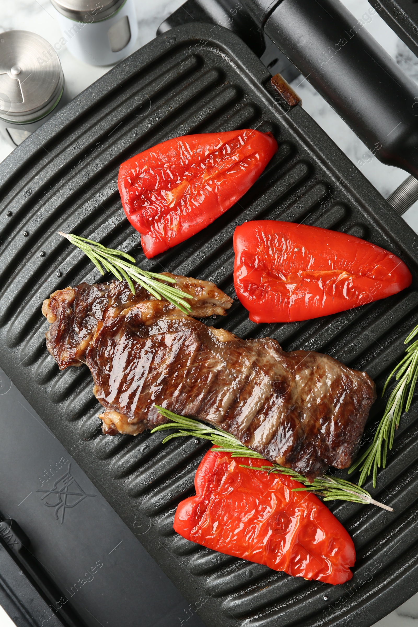Electric grill with beef steaks, bell peppers and rosemary on white table, top view Photo of Electric grill with beef steaks, bell peppers and rosemary on white table, top view