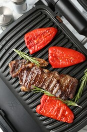 Photo of Electric grill with beef steaks, bell peppers and rosemary on white table, top view