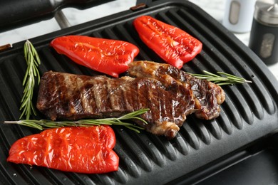 Photo of Electric grill with beef steaks, bell peppers and rosemary on white table, closeup