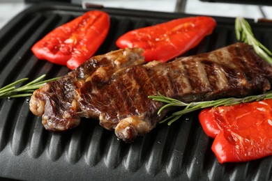 Photo of Electric grill with beef steaks, bell peppers and rosemary on white table, closeup
