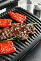 Photo of Electric grill with beef steaks, bell peppers and rosemary on white table, closeup