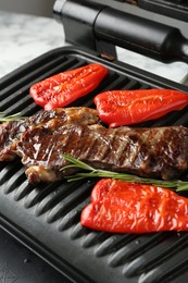 Photo of Electric grill with beef steaks, bell peppers and rosemary on white table, closeup