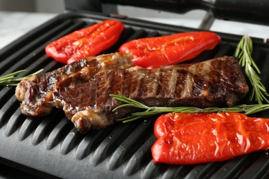 Photo of Electric grill with beef steaks, bell peppers and rosemary on white table, closeup