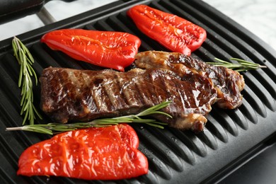Photo of Electric grill with beef steaks, bell peppers and rosemary on white table, closeup