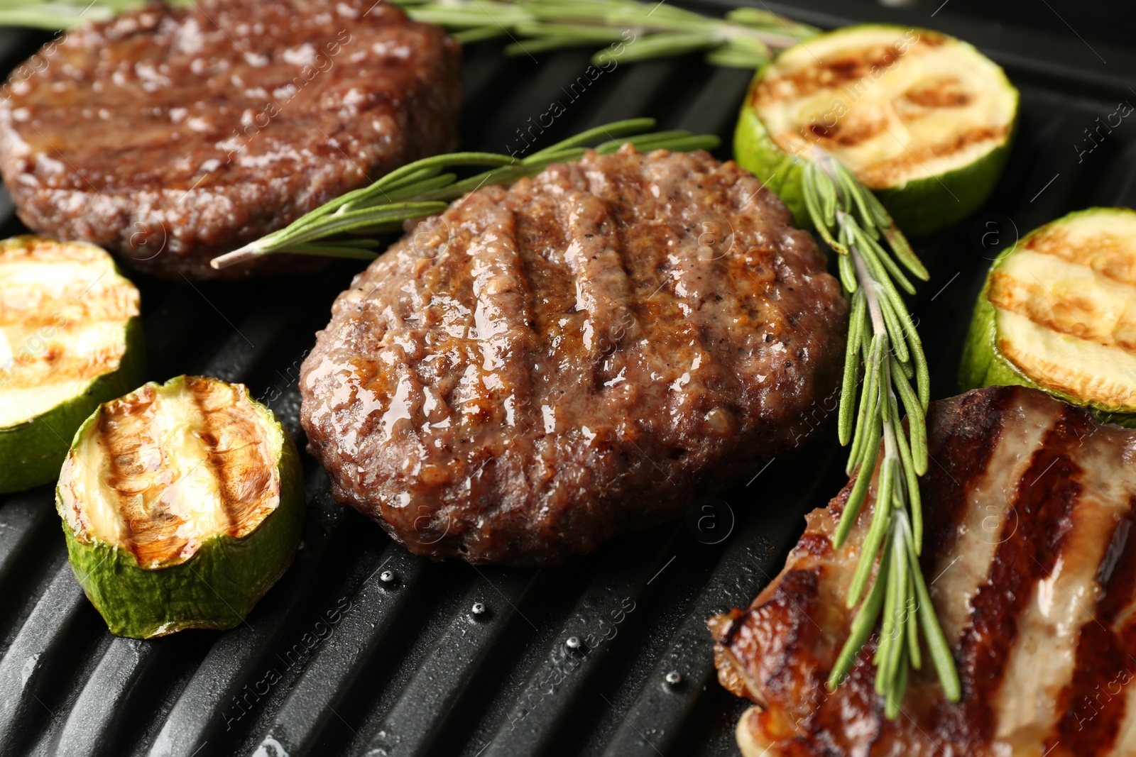 Photo of Electric grill with beef steaks, zucchini and rosemary, closeup