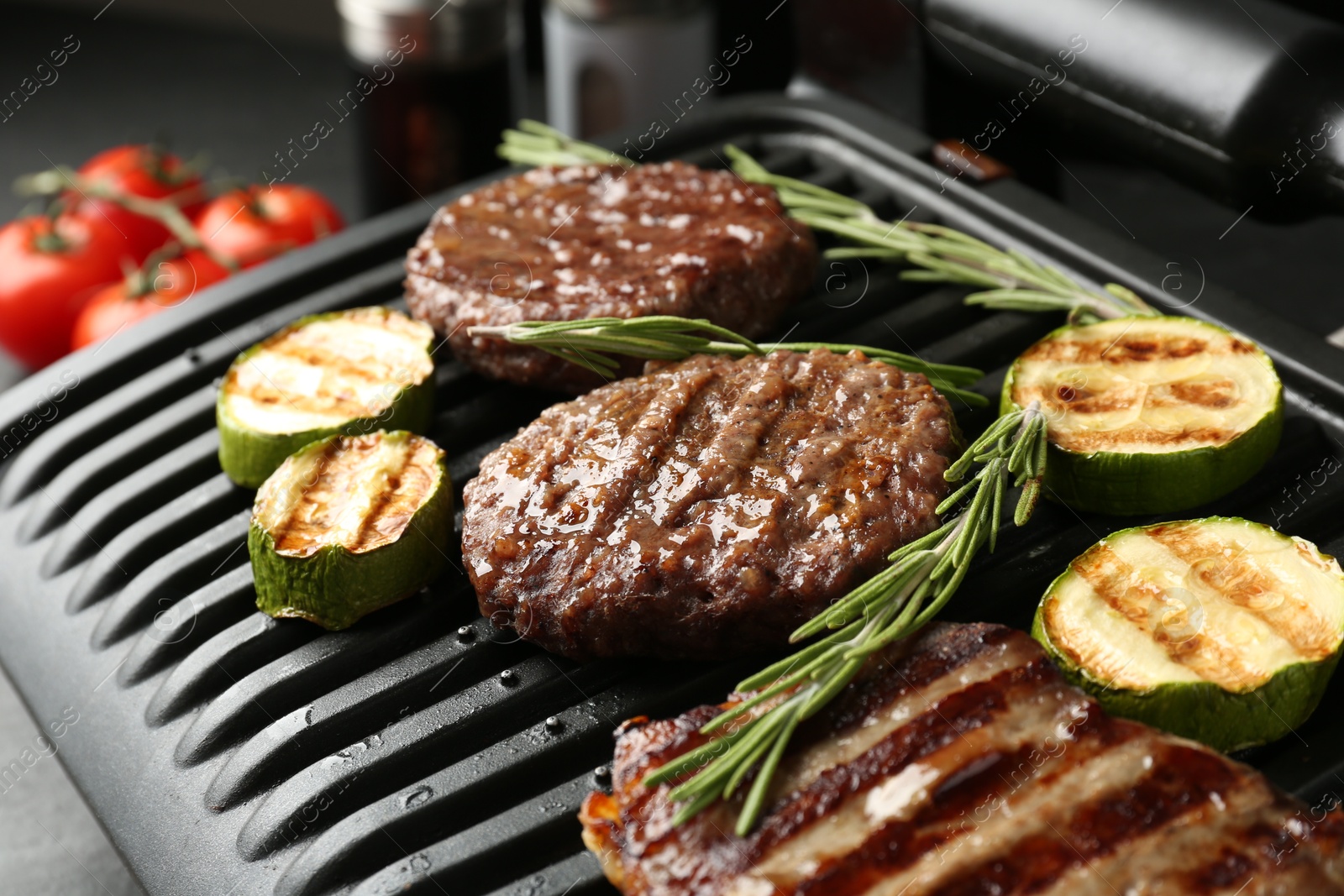 Photo of Electric grill with beef steaks, zucchini and rosemary on black table, closeup