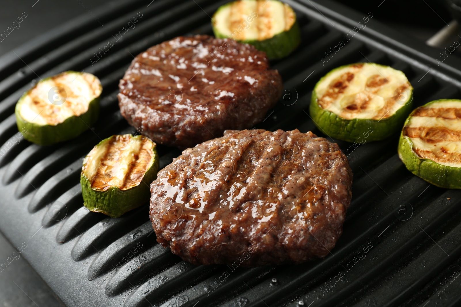 Photo of Electric grill with beef and zucchini on black table, closeup
