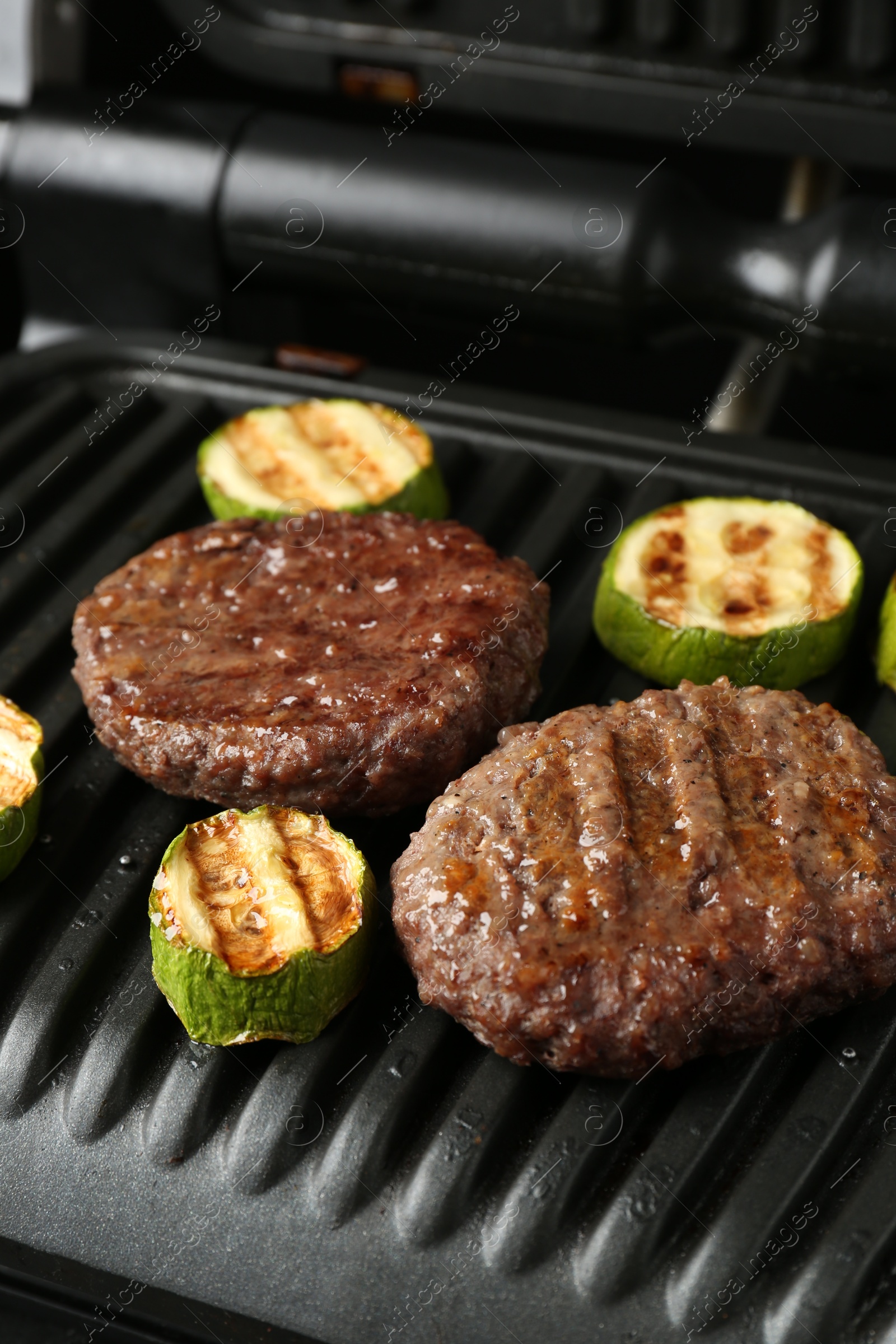 Photo of Electric grill with beef and zucchini on black table, closeup