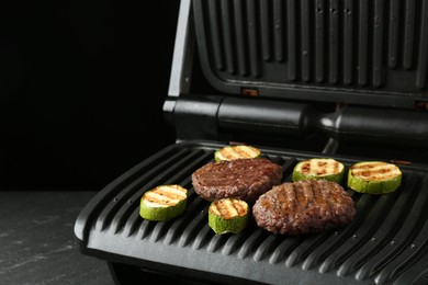 Photo of Electric grill with beef and zucchini on black table, closeup
