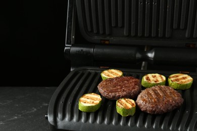 Photo of Electric grill with beef and zucchini on black table, closeup