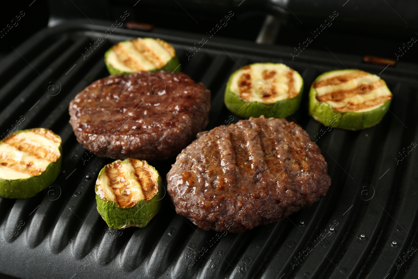 Photo of Electric grill with beef and zucchini on black table, closeup