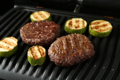 Photo of Electric grill with beef and zucchini on black table, closeup
