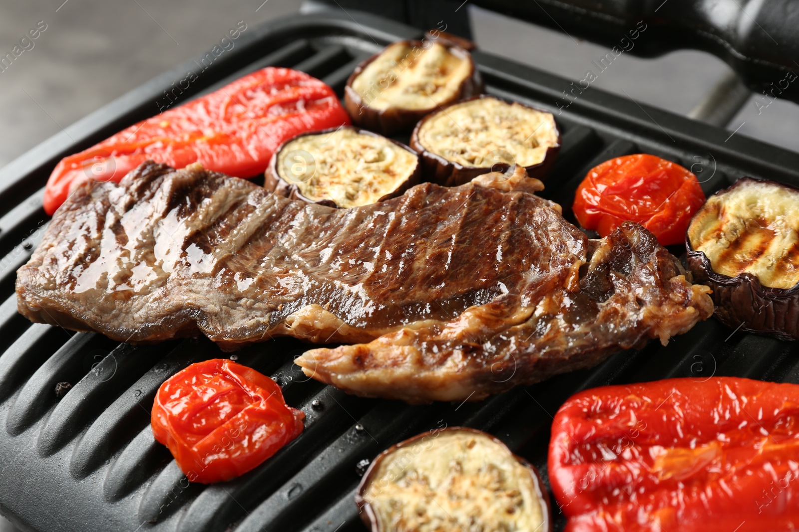 Photo of Electric grill with beef steaks and vegetables on grey table, closeup