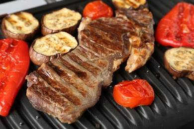 Photo of Electric grill with beef steaks and vegetables on grey table, closeup