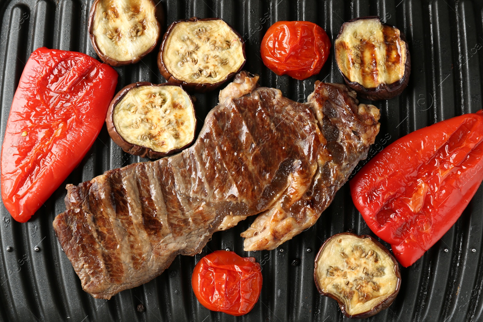 Photo of Electric grill with beef steaks and vegetables, closeup