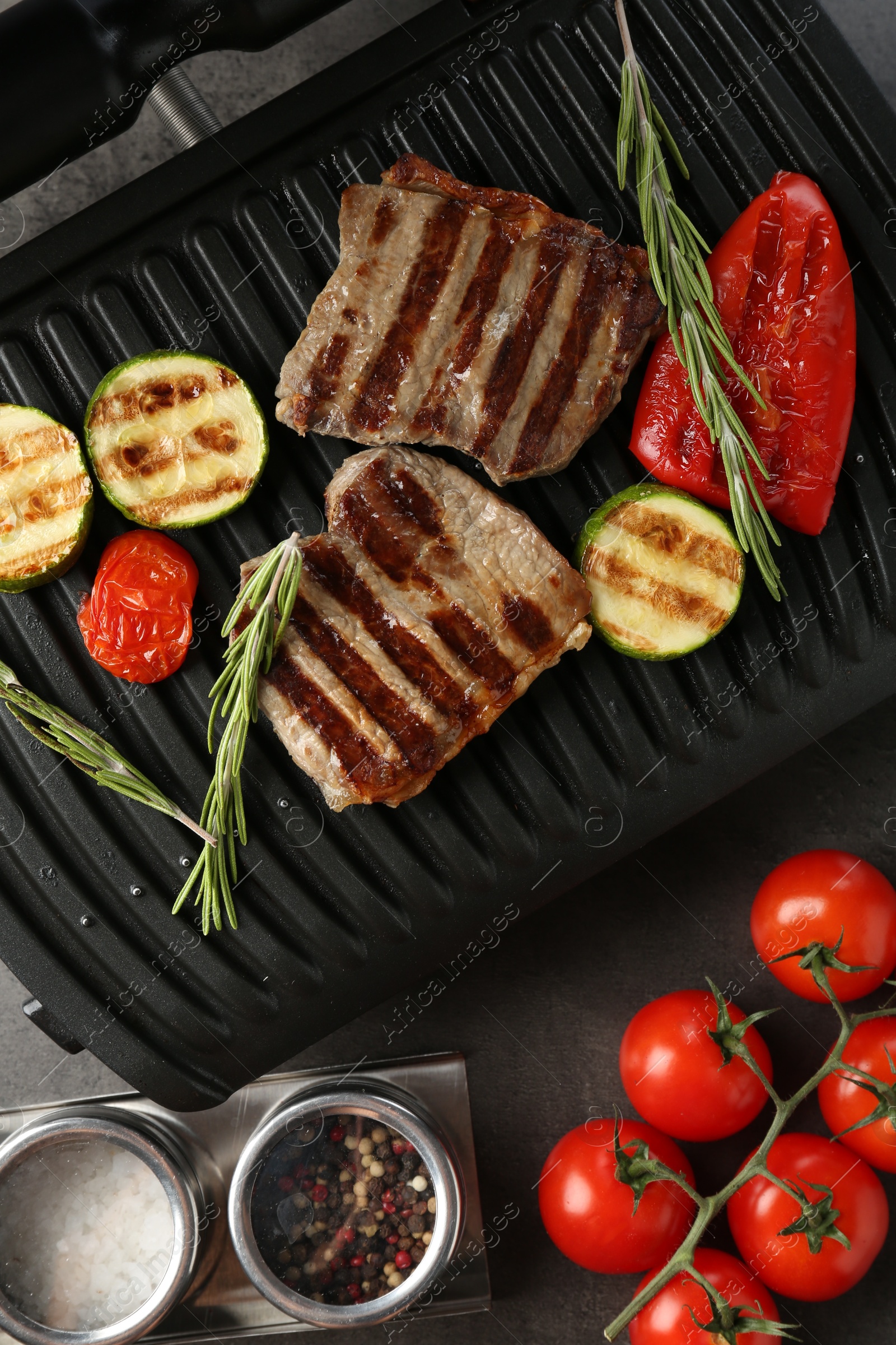 Photo of Electric grill with beef steaks, vegetables and rosemary on grey table, flat lay