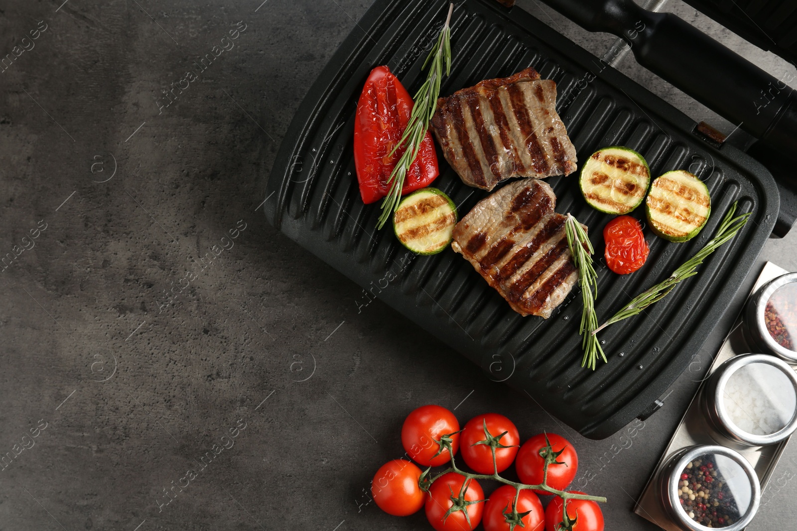 Electric grill with beef steaks, vegetables and rosemary on grey table, flat lay. Space for text Photo of Electric grill with beef steaks, vegetables and rosemary on grey table, flat lay. Space for text