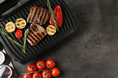 Photo of Electric grill with beef steaks, vegetables and rosemary on grey table, flat lay. Space for text