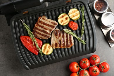Photo of Electric grill with beef steaks, vegetables and rosemary on grey table, flat lay