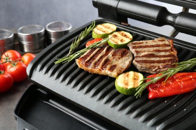 Photo of Electric grill with beef steaks, vegetables and rosemary on grey table, closeup