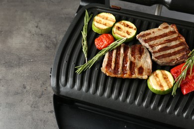 Photo of Electric grill with beef steaks, vegetables and rosemary on grey table, closeup