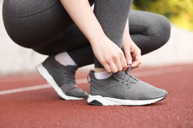 Photo of Runner tying shoelace of her sneaker outdoors, closeup