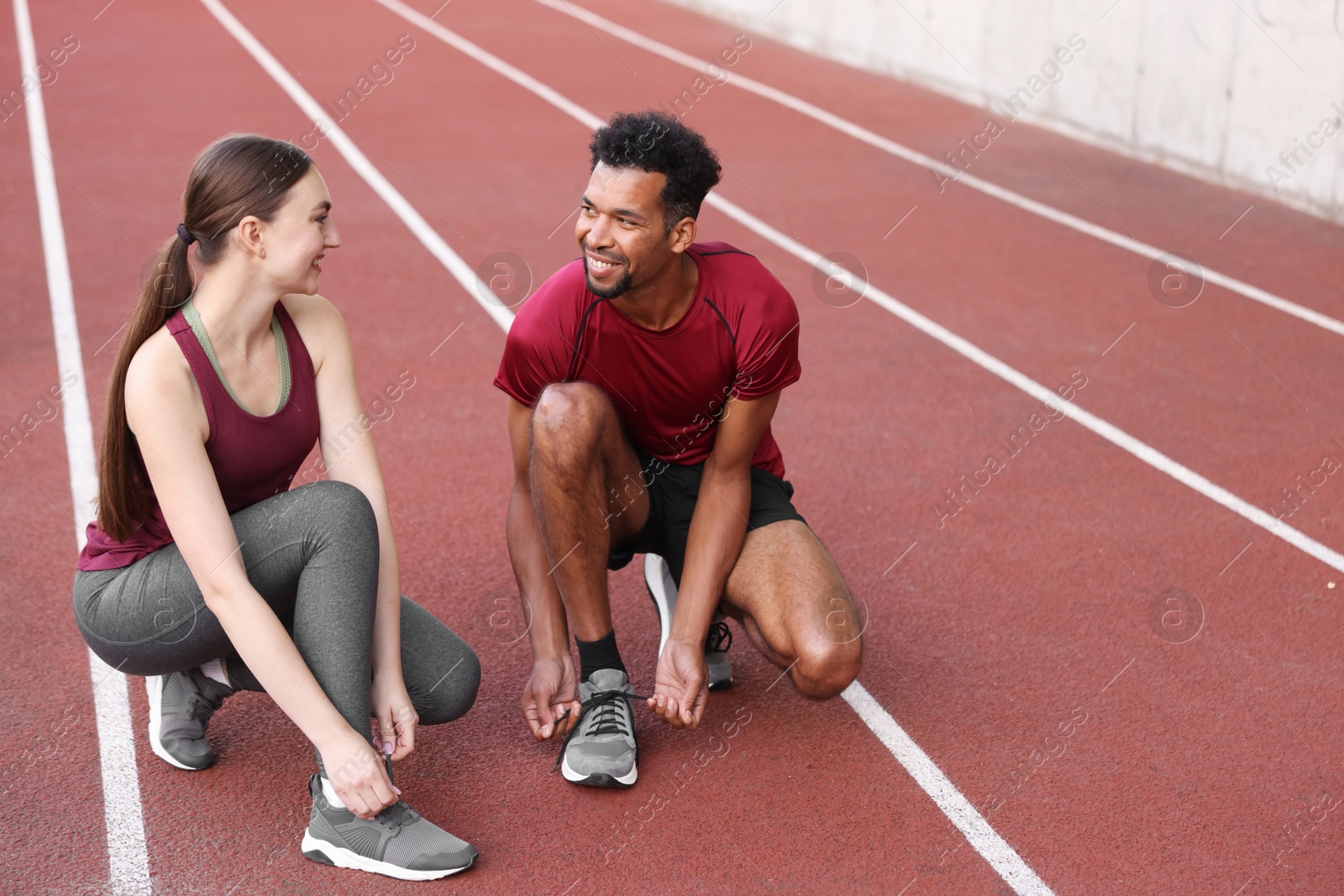 Photo of Smiling runners tying shoelaces of their sneakers at stadium. Space for text