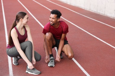 Photo of Smiling runners tying shoelaces of their sneakers at stadium. Space for text
