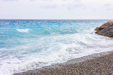 Photo of Beautiful view of wavy sea, rocks and pebbles on beach