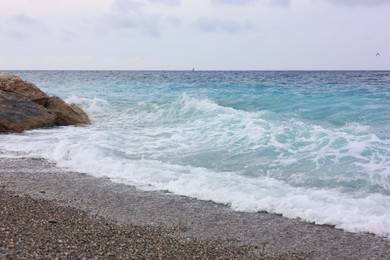 Photo of Beautiful view of wavy sea, rocks and pebbles on beach
