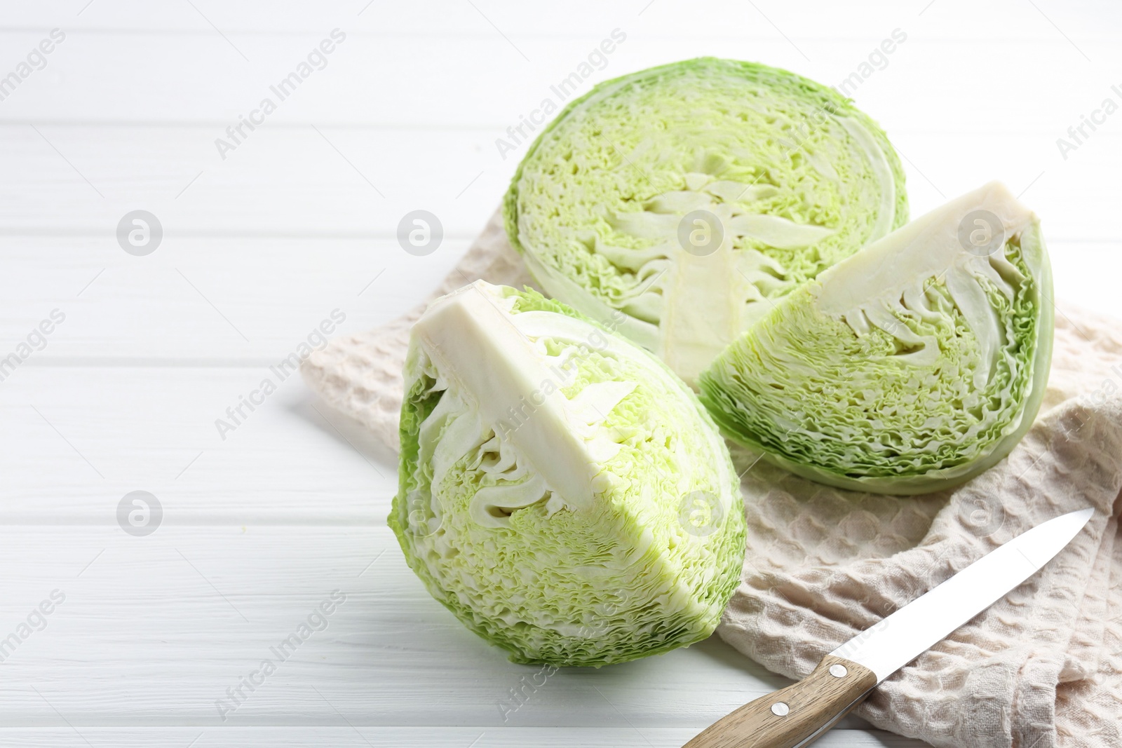 Photo of Fresh cut Savoy cabbage and knife on white wooden table, closeup. Space for text