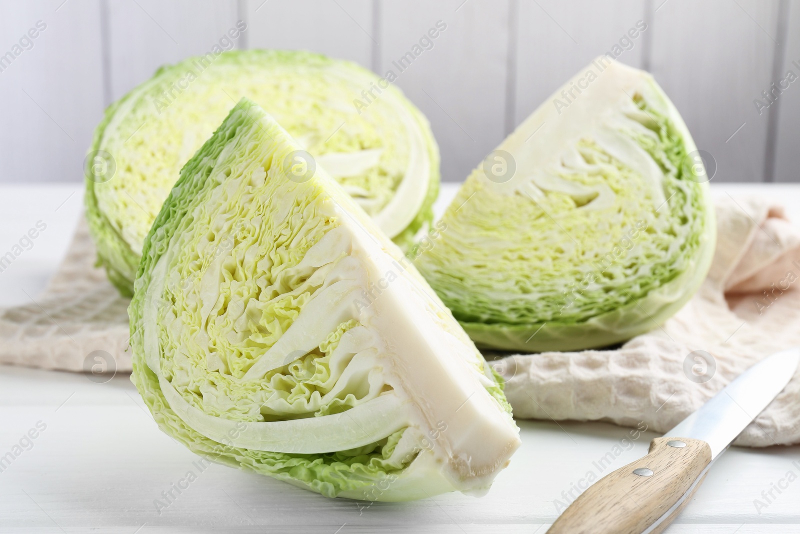 Photo of Fresh cut Savoy cabbage and knife on white wooden table, closeup