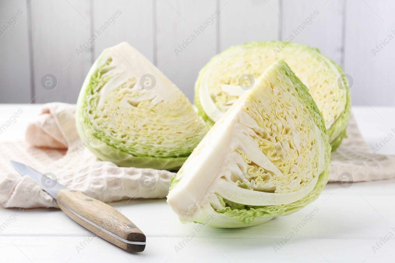 Photo of Fresh cut Savoy cabbage and knife on white wooden table, closeup