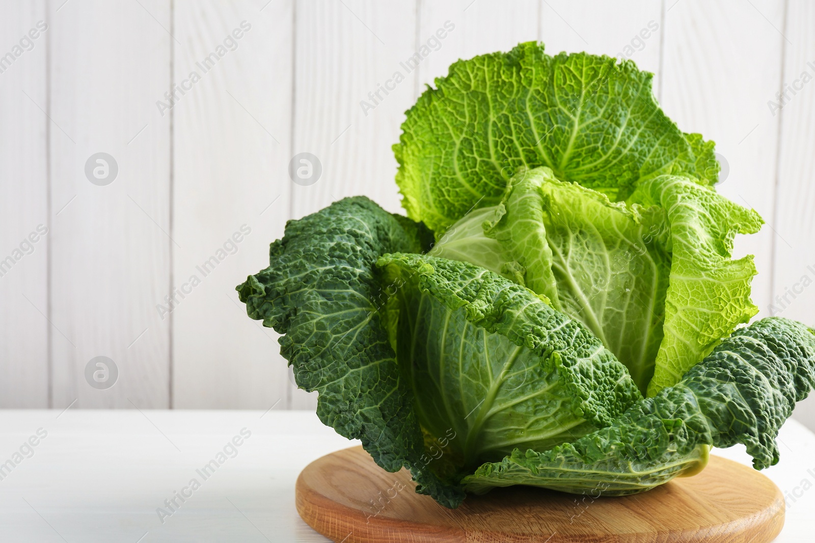 Photo of One fresh Savoy cabbage on white wooden table, closeup. Space for text