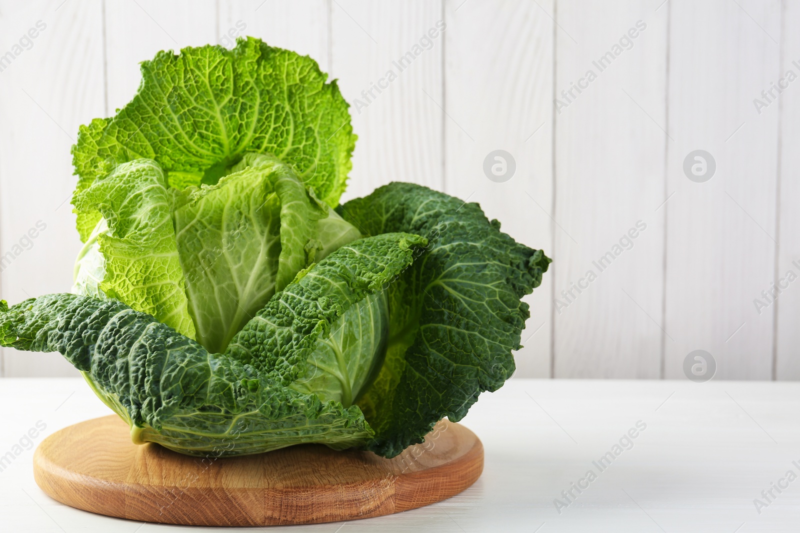 Photo of One fresh Savoy cabbage on white wooden table, closeup. Space for text