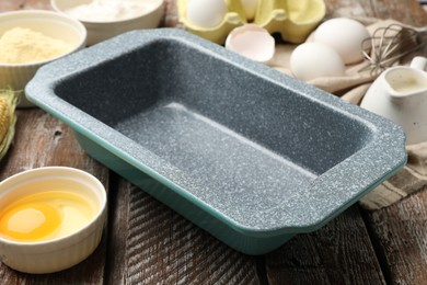 Photo of Making cornbread. Baking dish and different ingredients on wooden table, closeup
