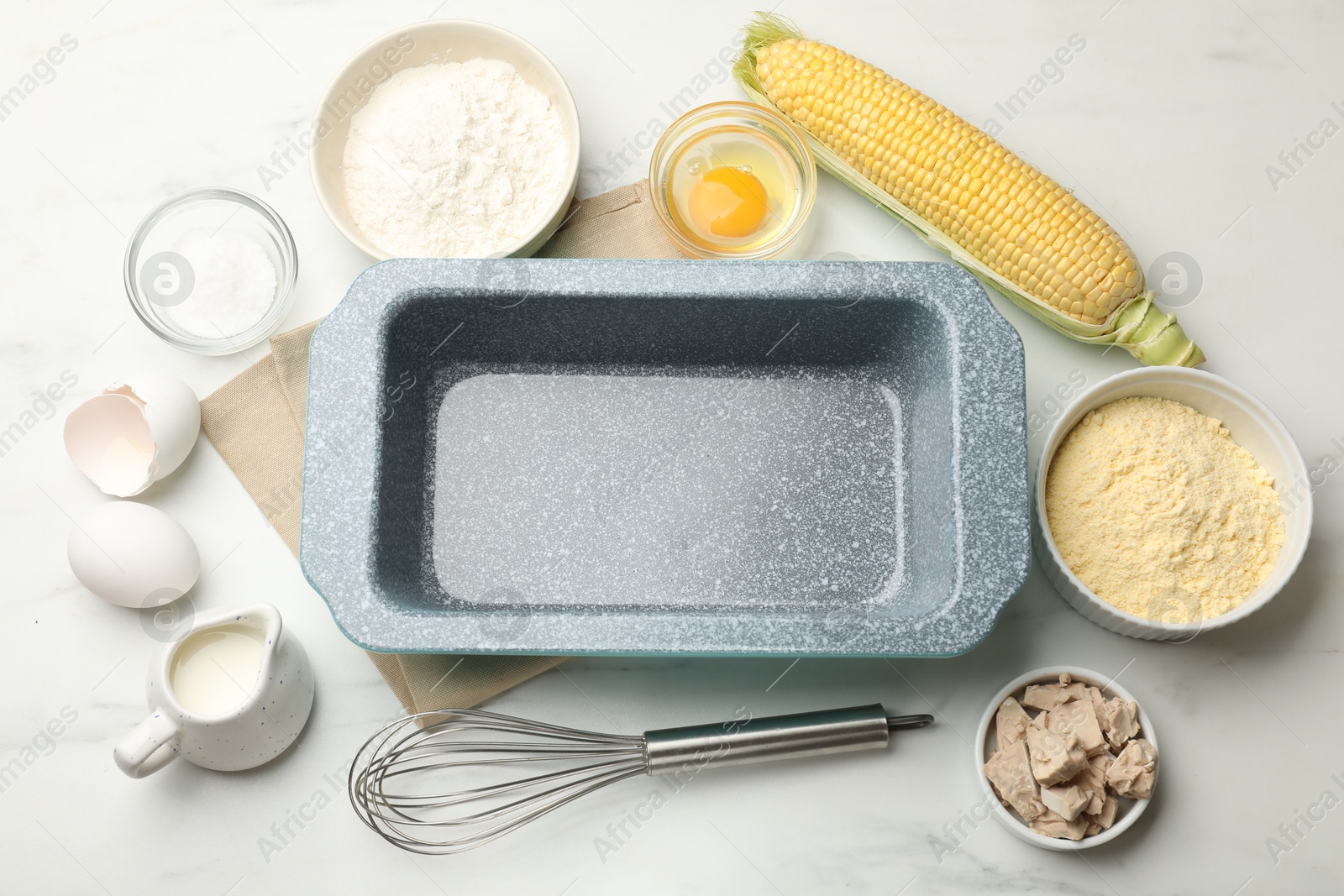 Making cornbread. Baking dish surrounded by different ingredients and whisk on white marble table, flat lay Photo of Making cornbread. Baking dish surrounded by different ingredients and whisk on white marble table, flat lay