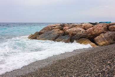 Photo of Beautiful view of wavy sea, rocks and pebbles on beach