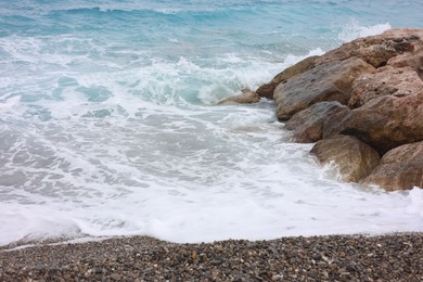 Photo of Beautiful view of wavy sea, rocks and pebbles on beach