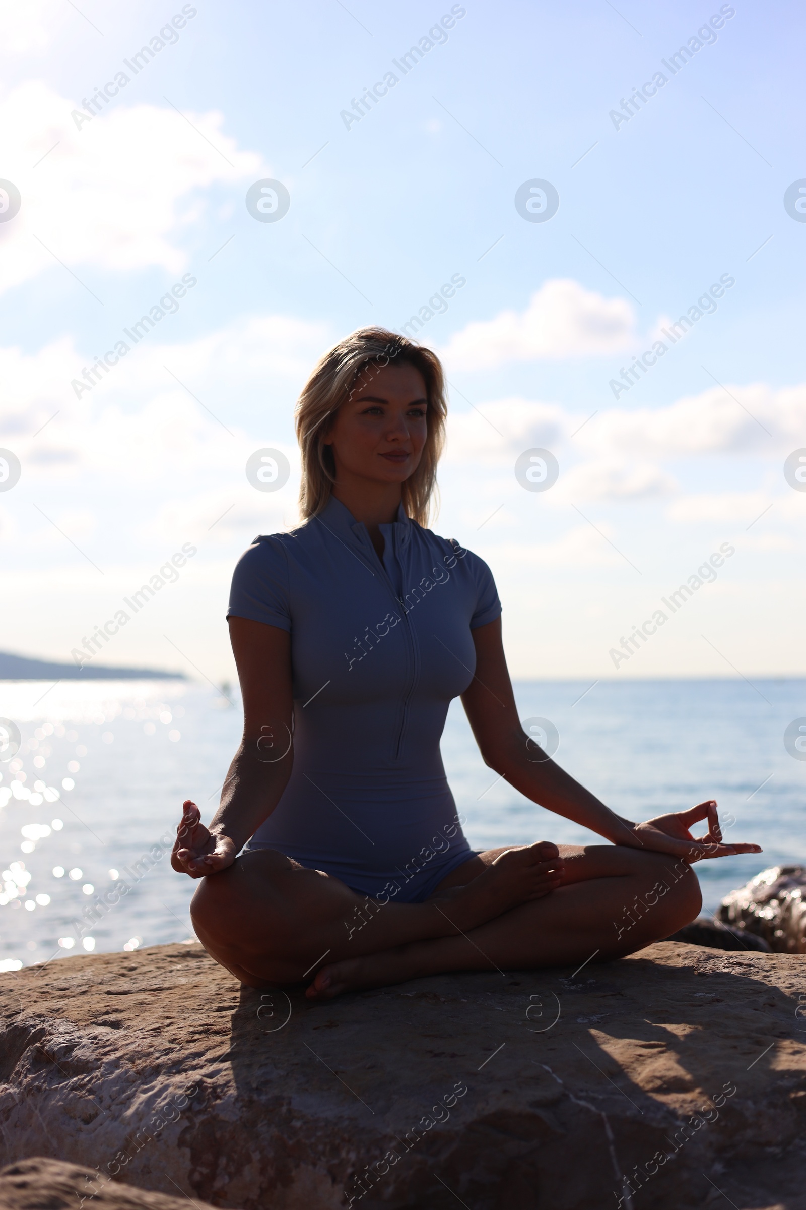 Photo of Young woman in sportswear practicing yoga on rocks at beach