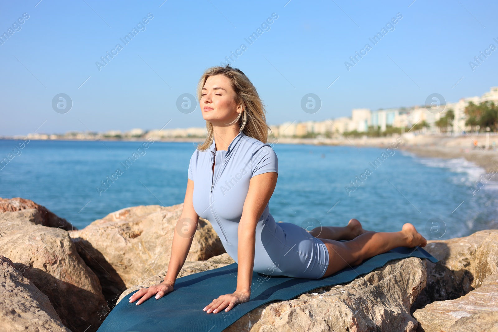 Photo of Young woman in sportswear practicing yoga on rocks at beach