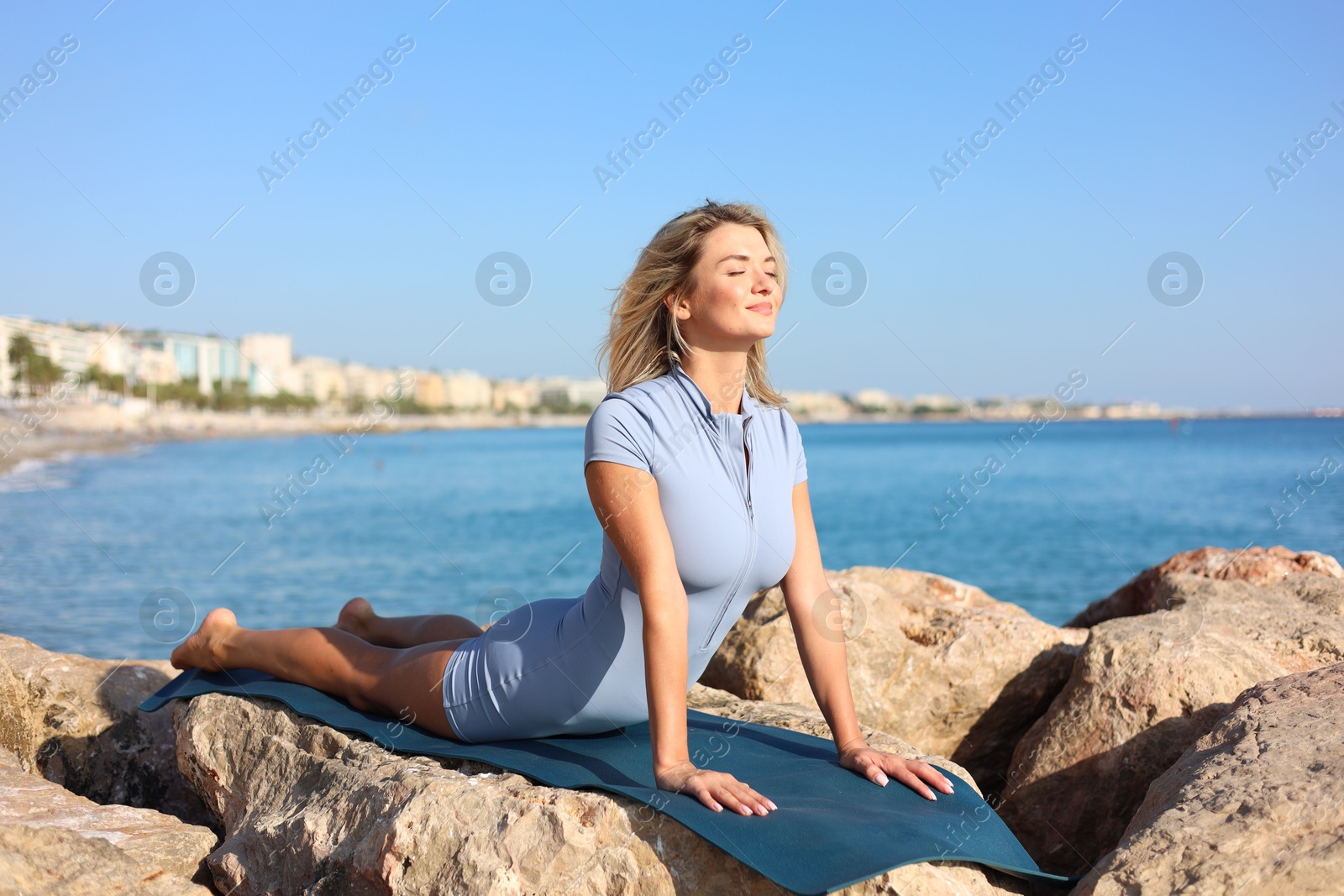 Photo of Young woman in sportswear practicing yoga on rocks at beach