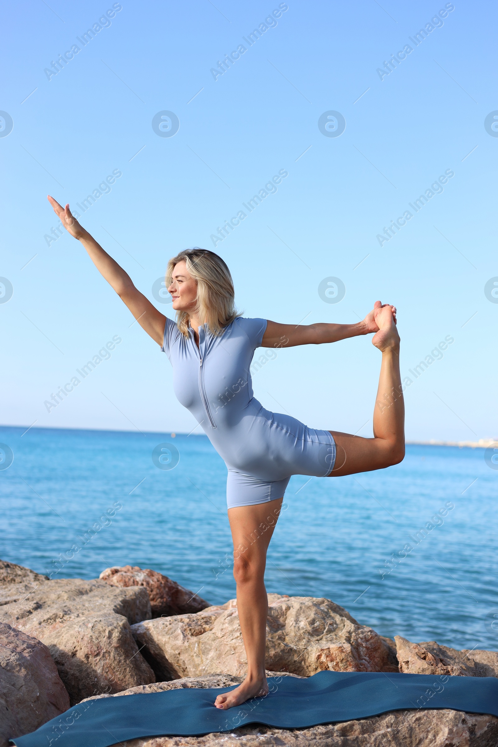 Photo of Young woman in sportswear practicing yoga on rocks at beach