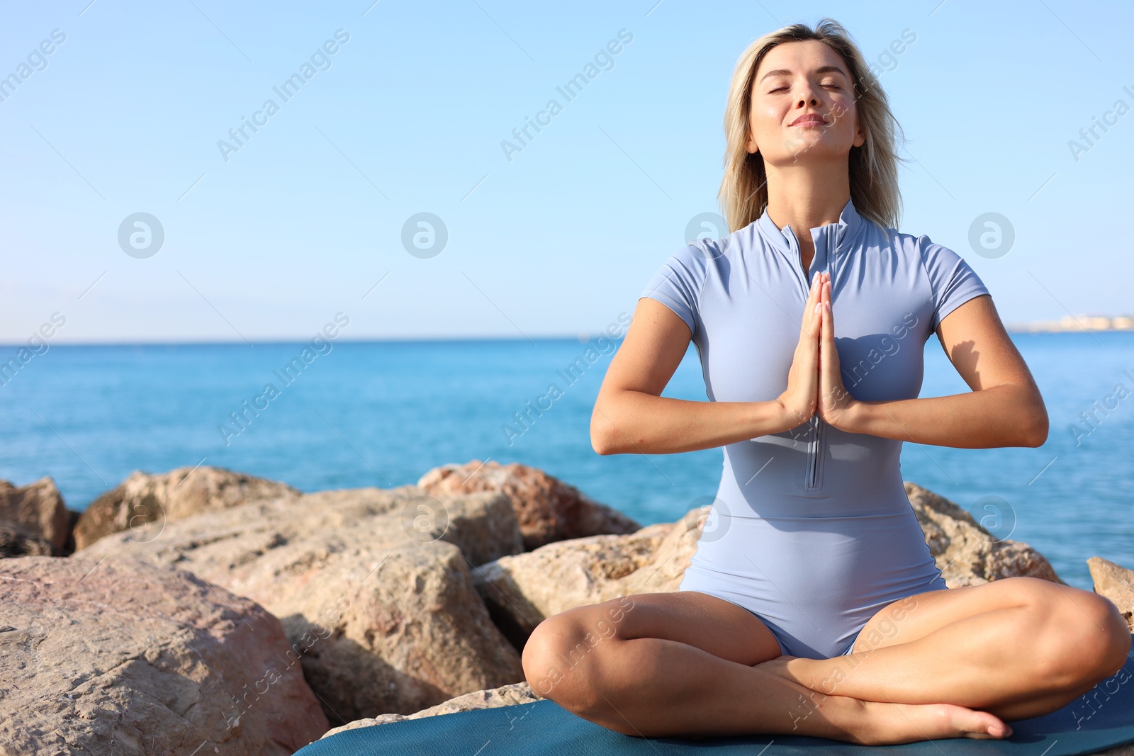 Photo of Young woman in sportswear practicing yoga on rocks at beach, space for text